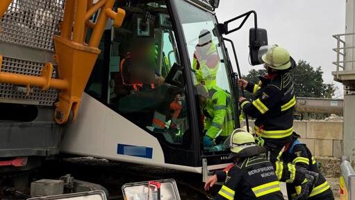 Feuerwehrleute helfen dem Kranführer aus der Kabine. Er kann sich vor Schmerzen kaum bewegen.