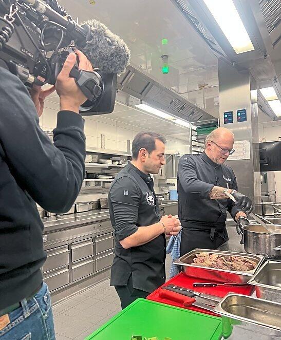 Promi-Koch Ali G&uuml;ng&ouml;rm&uuml;s (M.) schaut Donisl-K&uuml;chenchef Rainer Unglaub (r.) &uuml;ber die Schulter.