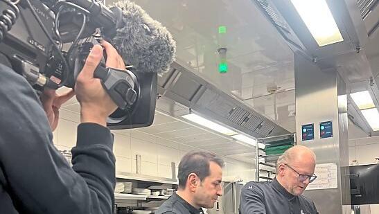 Promi-Koch Ali G&uuml;ng&ouml;rm&uuml;s (M.) schaut Donisl-K&uuml;chenchef Rainer Unglaub (r.) &uuml;ber die Schulter.
