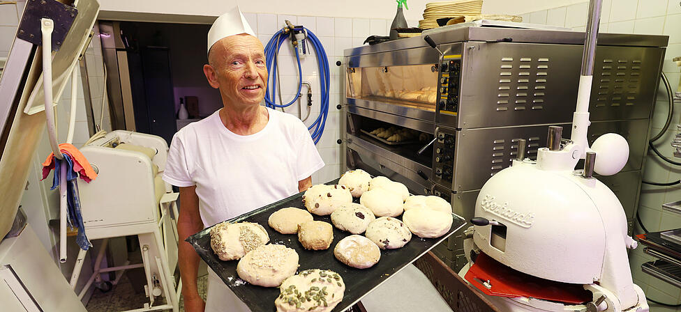 B&auml;cker Artur Herrmann pr&auml;sentiert in seiner kleinen Backstube ein Blech frisch geformter Semmeln, bevor sie in den Ofen geschoben werden.