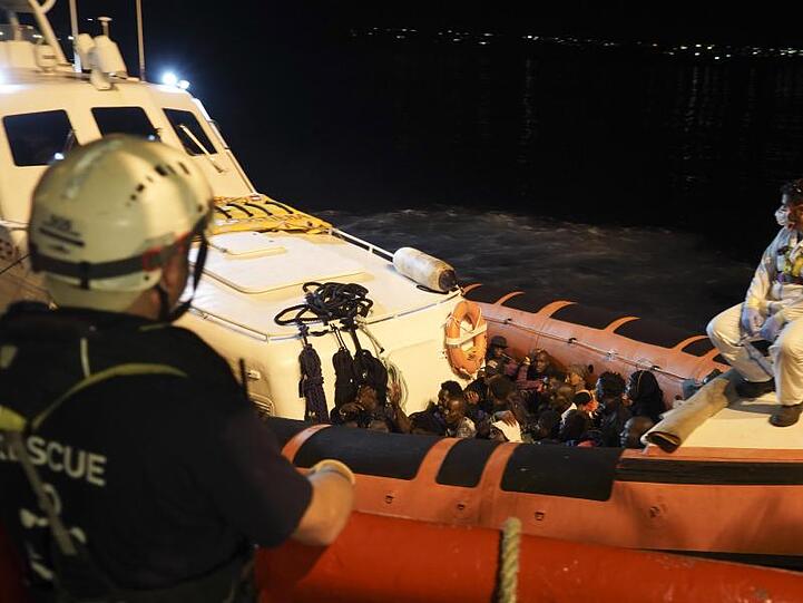 Migranten sitzen in einem Boot der italienischen Küstenwache, nachdem sie von Bord des Rettungsschiffs "Ocean Viking" gegangen sind.