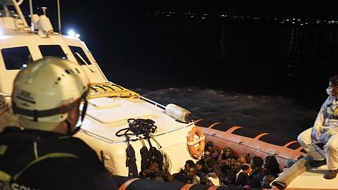 Migranten sitzen in einem Boot der italienischen Küstenwache, nachdem sie von Bord des Rettungsschiffs "Ocean Viking" gegangen sind.