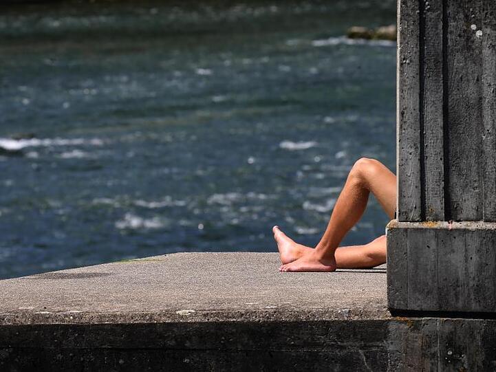Ein junger Mann sitzt am Lechwehr bei sommerlichen Temperaturen. Foto: Karl-Josef Hildenbrand/dpa/Archivbild