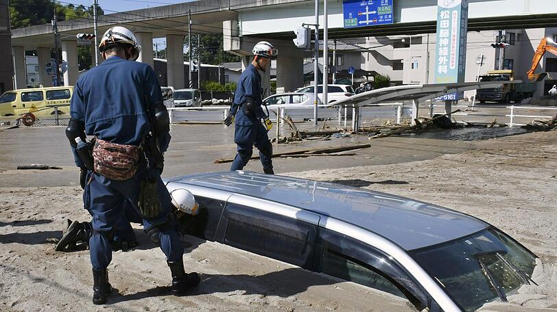 Japan, Kure: Ein Polizist inspiziert während einer Suchaktion ein Auto, das von Schlamm begraben ist, nachdem es nach schweren Regenfällen zu Erdrutschen und Überschwemmungen kam. Nach den verheerenden Überschwemmungen in Japan werden noch immer zahlreiche Menschen vermisst.