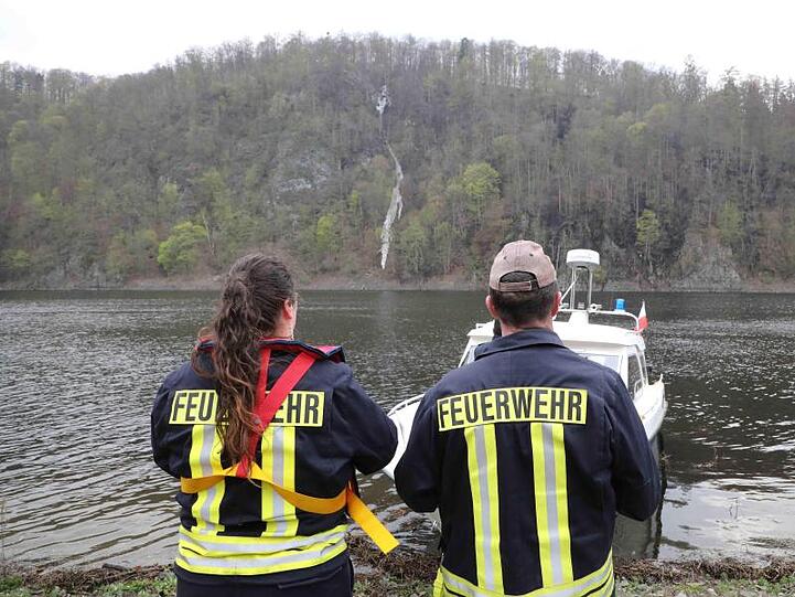 Feuerwehrleute stehen bei einem Brand im Wald an der Bleilochtalsperre am Rande des Wassers. Foto: Bodo Schackow
