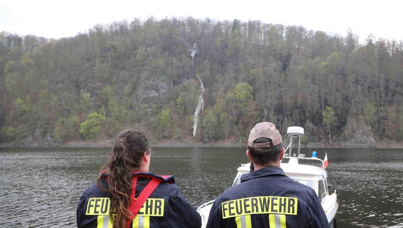 Feuerwehrleute stehen bei einem Brand im Wald an der Bleilochtalsperre am Rande des Wassers. Foto: Bodo Schackow Feuerwehrleute stehen bei einem Brand im Wald an der Bleilochtalsperre am Rande des Wassers. Foto: Bodo Schackow