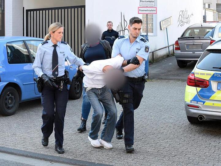 Ein mutmaßlich Verdächtiger wird von Polizeibeamten abgeführt, im Hintergrund eine Zivilfahnderin der Polizei.