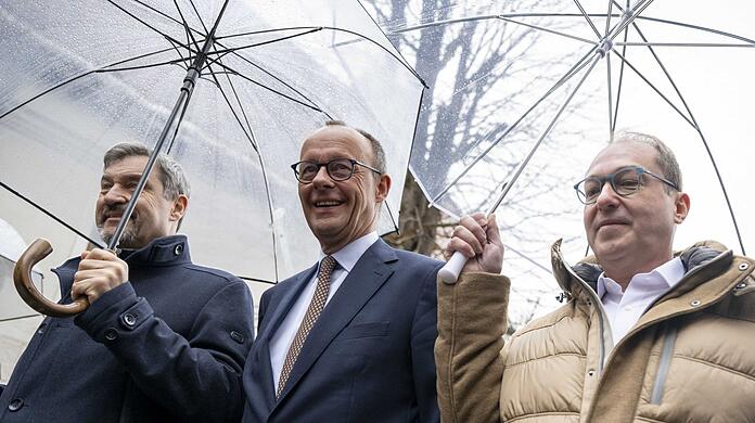 Nachdem er Markus Söder (l.) und Alexander Dobrindt (r.) hat warten lassen, schützen sie ihn mit ihren Schirmen vor dem Regen.