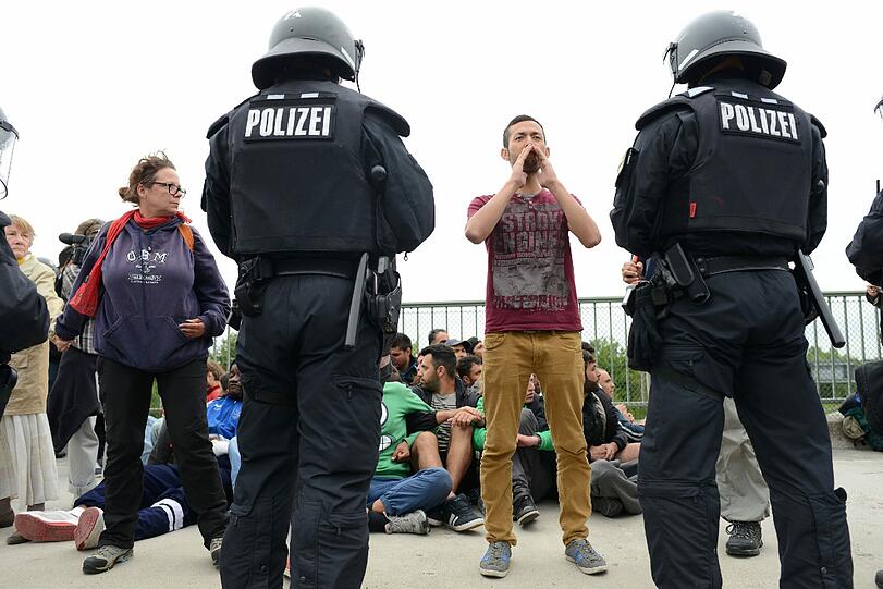 Auf einer Brücke über die A99 werden die Flüchtlinge am Montagnachmittag kurz hinter Dachau aufgehalten. Als die Beamten versuchen, einzelne Demonstranten aus der Menschenkette zu holen, kommt es zu Auseinandersetzungen, bei denen einige Personen verletzt werden.