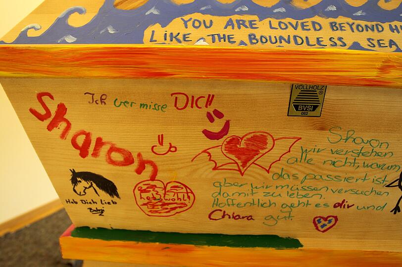 "Sharon, wir wissen alle nicht, warum das passiert ist, aber wir müssen versuchen damit zu leben. Hoffentlich geht es Dir und Chiara gut", steht in zarten grünen Buchstaben auf der Schmalseite des Sarges.
