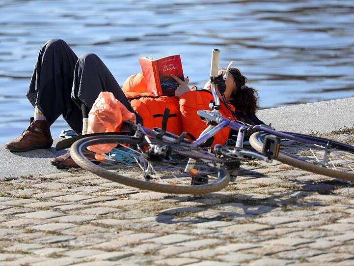 Frühling im Februar: Eine Frau liegt bei Temperaturen um 14 Grad Celsius im Berliner Regierungsviertel am Ufer der Spree.