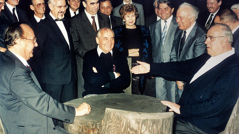 Legendäre Männerrunde: Helmut Kohl mit dem sowjetischen Präsidenten Michail Gorbatschow (M.) und Bundesaußenminister Hans-Dietrich Genscher an einem rustikalen Arbeitstisch in der freien russischen Natur.