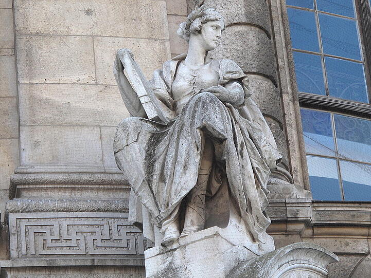 Neben dieser Statue sieht man eine schörkelige Verzierung an der Fassade des Justizpalastes. Bei genauerem Hinsehen...