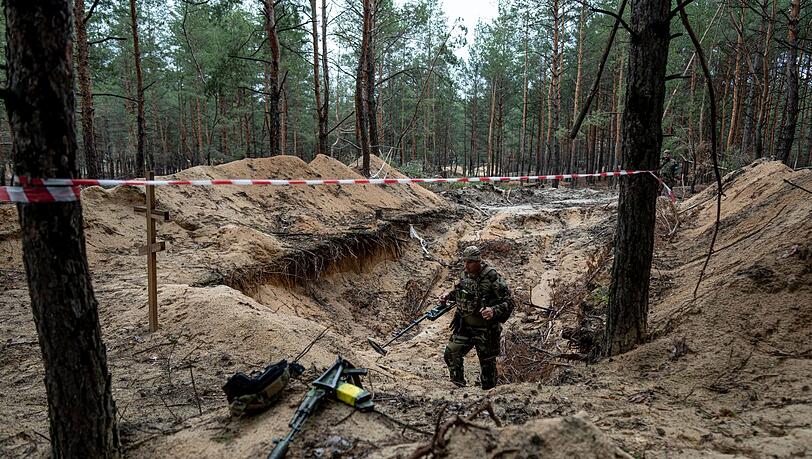 Ein ukrainischer Soldat inspiziert mit einem Metalldetektor ein Massengrab in der kürzlich zurückeroberten Stadt Isjum.