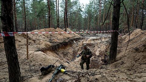 Ein ukrainischer Soldat inspiziert mit einem Metalldetektor ein Massengrab in der kürzlich zurückeroberten Stadt Isjum.