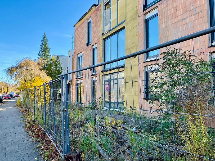 Nur wenige Fenster sind noch abgeklebt. Vor dem Gebäude wuchert das Gebüsch.