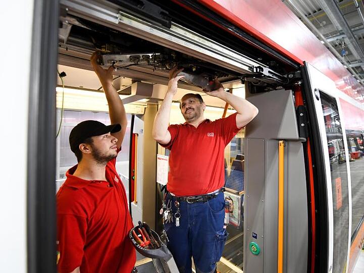 Furkan Gülkaya (l) und Ömer Yenidede, Mitarbeiter der DB, tauschen bei einem Zug eine Türsteuerungseinheit. Foto: Tobias Hase/Archivbild