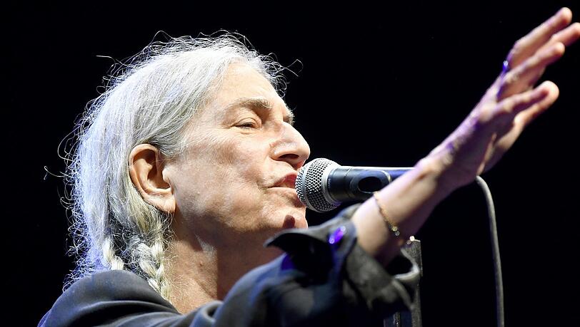 Mit einem lässig-schlabbrigen schwarzen Dreiteiler und zwei Zöpfen an jeder Seite: Patti Smith in der Tollwood Musikarena.