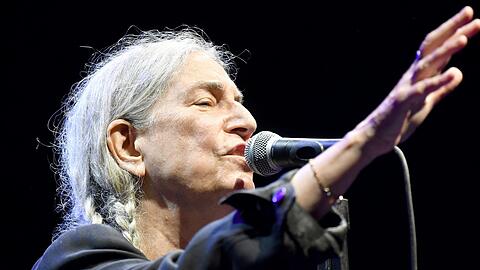 Mit einem lässig-schlabbrigen schwarzen Dreiteiler und zwei Zöpfen an jeder Seite: Patti Smith in der Tollwood Musikarena.