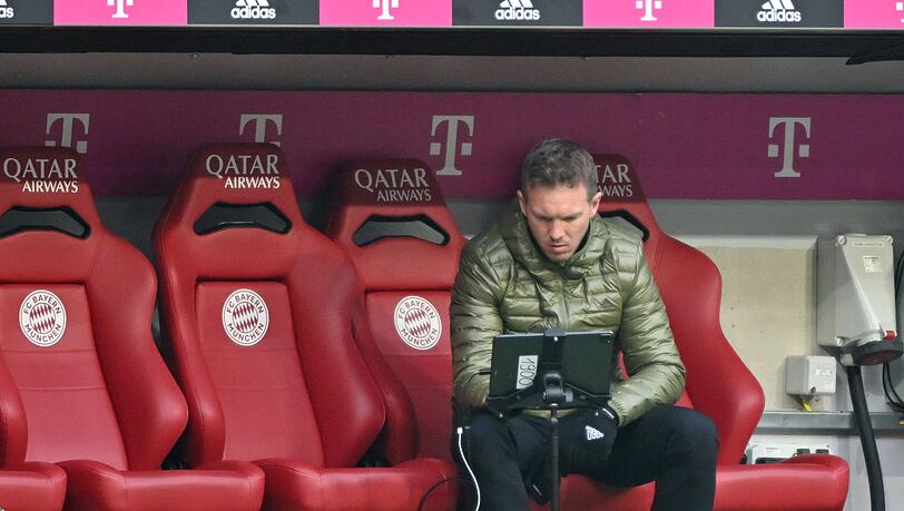 Münchens Trainer Julian Nagelsmann vom FC Bayern München sitzt in der Halbzeit auf der Trainerbank und schaut auf einen Bildschirm.