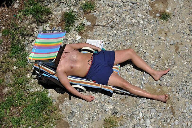 Dieser Mann hat Schutzvorkehrungen getroffen. Er sonnt sich an der Isar. Temperaturen um die 30 Grad lockten in den vergangenen Tagen in ganz Bayern die Menschen in Freibäder, Biergärten und Straßencafes.