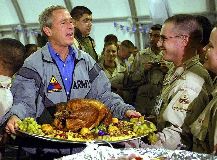 Der Turkey war getürkt: US-Präsident George W. Bush hält am 27.11.2003 auf dem Flughafen von Bagdad bei einem Thanksgiving-Essen mit etwa 600 Soldaten eine Platte mit einem Dekorations-Truthahn in Händen.