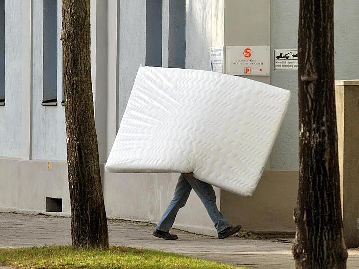 Ein Mann trägt eine Matratze. Foto: Armin Weigel/dpa