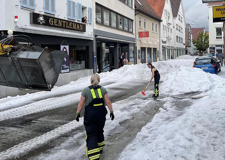 Einsatzkräfte der Feuerwehr räumen Hagel von einer Straße.