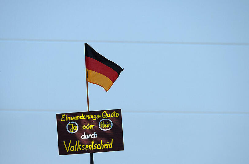 Demonstranten halten in Heidenau während des Besuches von Bundeskanzlerin Merkel gegenüber der Flüchtlingsunterkunft ein Schild mit dem Schriftzug "Einwanderungs-Quote ja oder nein durch Volksentscheid" hoch.