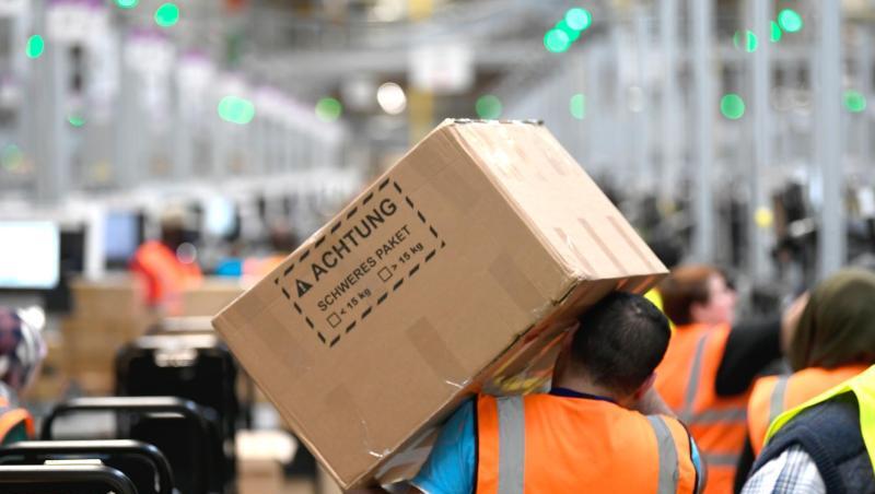 Ein Mitarbeiter trägt ein Paket im Logistikzentrum des Versandhändlers Amazon. Ein Mitarbeiter trägt ein Paket im Logistikzentrum des Versandhändlers Amazon.
