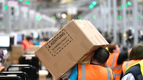 Ein Mitarbeiter trägt ein Paket im Logistikzentrum des Versandhändlers Amazon.