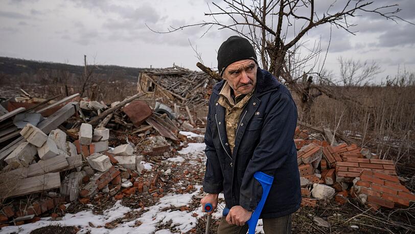 Andrii Cherednichenko (50), der von einer Landmine verletzt wurde, steht auf Krücken vor den Ruinen seines Hauses im ukrainischen Kamjanka.