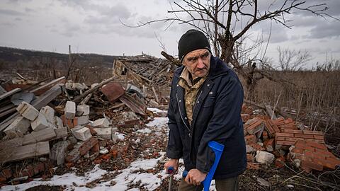 Andrii Cherednichenko (50), der von einer Landmine verletzt wurde, steht auf Krücken vor den Ruinen seines Hauses im ukrainischen Kamjanka.