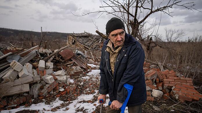 Andrii Cherednichenko (50), der von einer Landmine verletzt wurde, steht auf Krücken vor den Ruinen seines Hauses im ukrainischen Kamjanka.
