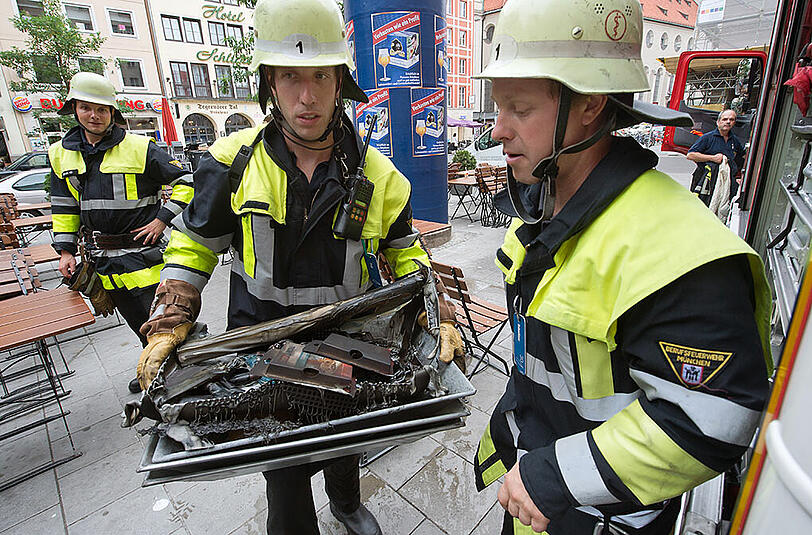 Explosion in Arztpraxis im Tal: Feuerwehrmänner tragen diverse verbrannte Gegenstände in einer Metallschale. Nach Angaben der Polizei wurden bei der Explosion drei Menschen verletzt, einer davon schwer.