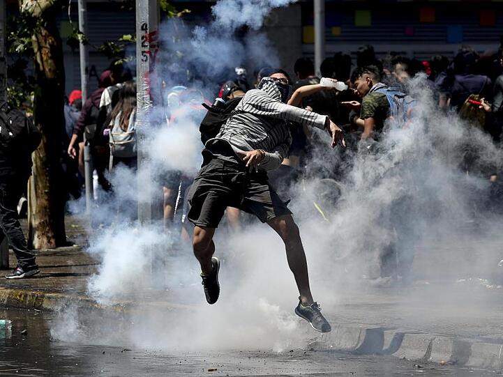 Ein Demonstrant wirft bei Protesten in Santiago de Chile eine Tränengasgranate zurück auf Polizisten.