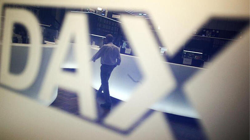 Ein Händler geht über das Parkett in der Börse in Frankfurt am Main und spiegelt sich dabei in einem Logo des Deutschen Aktienindexes (DAX).