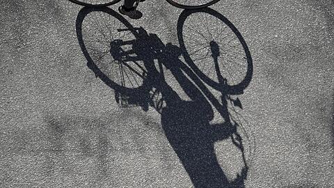 Ein Fahrradfahrer wirft einen langen Schatten auf den Asphalt einer Straße. Foto: Marcus Brandt/dpa/Symbolbild