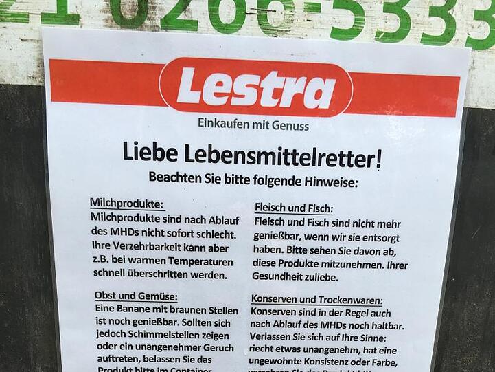 Ein Schild mit Hinweisen hängt zum sogenannten Containern an einem Müllcontainer am Kaufhaus Lestra.