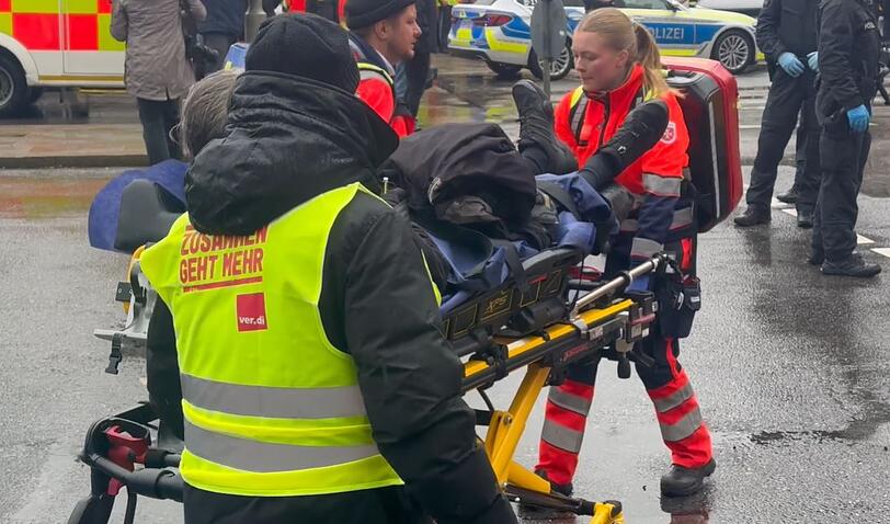 Ein Verletzter wird von Rettungskräften weggebracht. In der Münchner Innenstadt ist ein Fahrzeug in eine Menschengruppe gefahren. Wie die Polizei auf der Plattform X mitteilte, wurden mehrere Menschen verletzt.