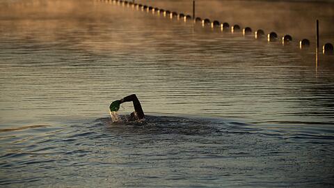 Ein Mann schwimmt am frühen Morgen in einem Badesee.