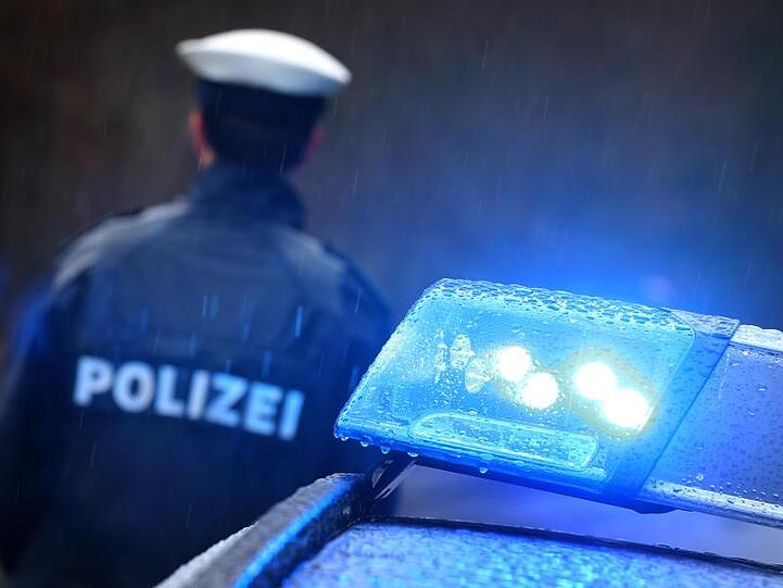 Ein Polizist steht im Regen vor einem Streifenwagen dessen Blaulicht aktiviert ist. Foto: Karl-Josef Hildenbrand/dpa/Archivbild