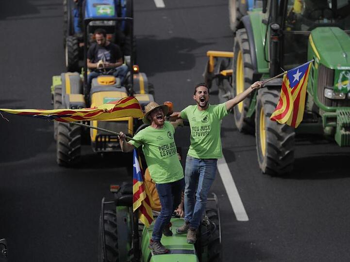 Demonstranten stehen auf einem Traktor und schwenken katalanische Fahnen.