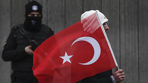 Ein Mann trägt in Istanbul eine türkische Fahne an einem Polizisten vorbei. Nach dem Anschlag sind nun die Personalien des Täters festgestellt worden.