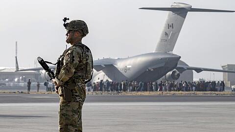 Ein Soldat der US-Luftwaffe steht auf dem Hamid Karzai International Airport in Kabul Wache. Vor den Toren des Flughafens stehen Tausende Menschen.