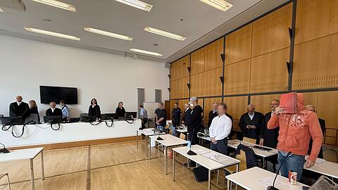 Die Angeklagten stehen im Sitzungssaal vor ihren Verteidigern.