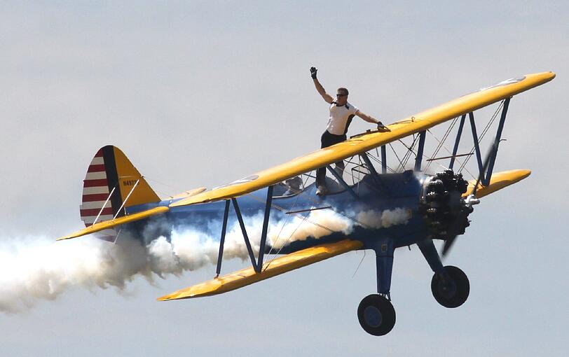 Todd Green winkt seinen Fans zu. Der "Wing Walker" ist es gewohnt, in luftigen Höhen umher zu spazieren. Sicherung oder Fallschirm trägt er nicht...