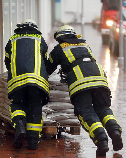 Feuerwehrmänner bringen in Westerland auf Sylt Sandsäcke in ein Haus