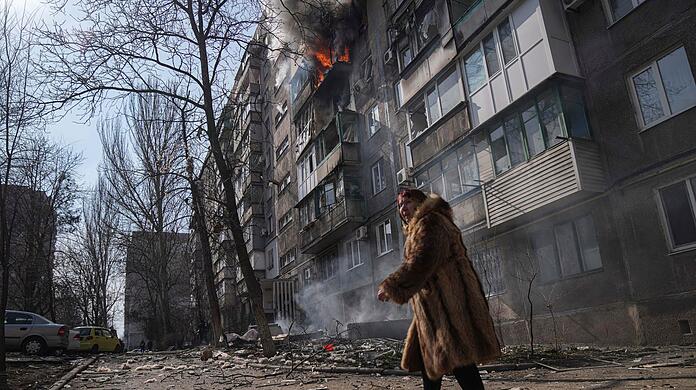 Szene aus Mariupol: Eine Frau geht an einem brennenden Wohnhaus vorbei, nachdem es beschossen wurde.