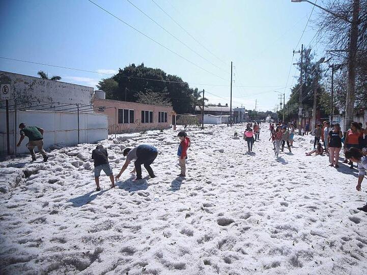 Kinder begutachten die dicke Hagelschicht auf einer Straße in der Stadt Guadalajara.